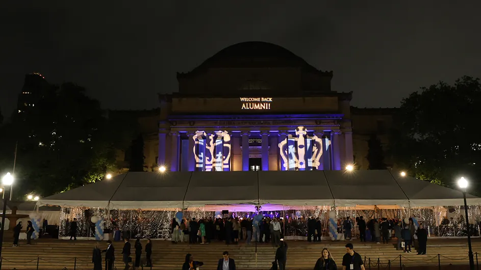 A tent filled with alumni underneath Low Library bearing lighting that reads "Welcome Back, Alumni!"