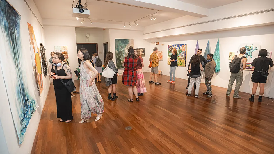 Several university students, faculty, and friends mingle, converse, and view art displayed on walls of LeRoy Neiman Gallery at Columbia University School of the Arts. 