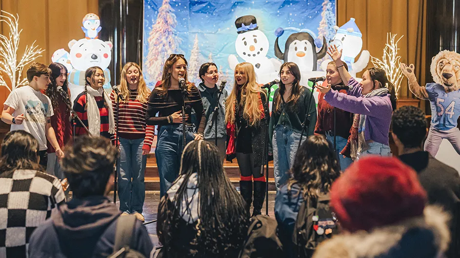Ten university students sing if front of a winter backdrop with an audience looking on in Low Library Rotunda at Columbia University. 