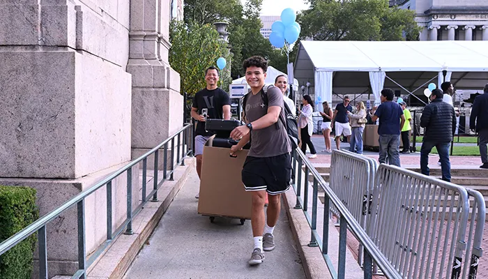 A student pulls a cart with luggage and move-in materials.