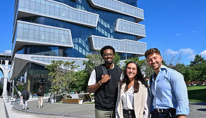 Three students pose in front of Kravis Hall