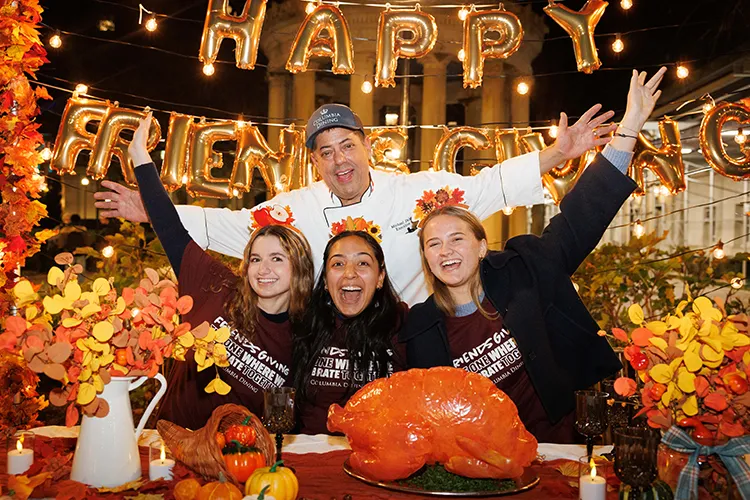Chef Mike and three university students smile and cheer at Columbia Dining's Friendsgiving display on Van Am Quad at Columbia University.