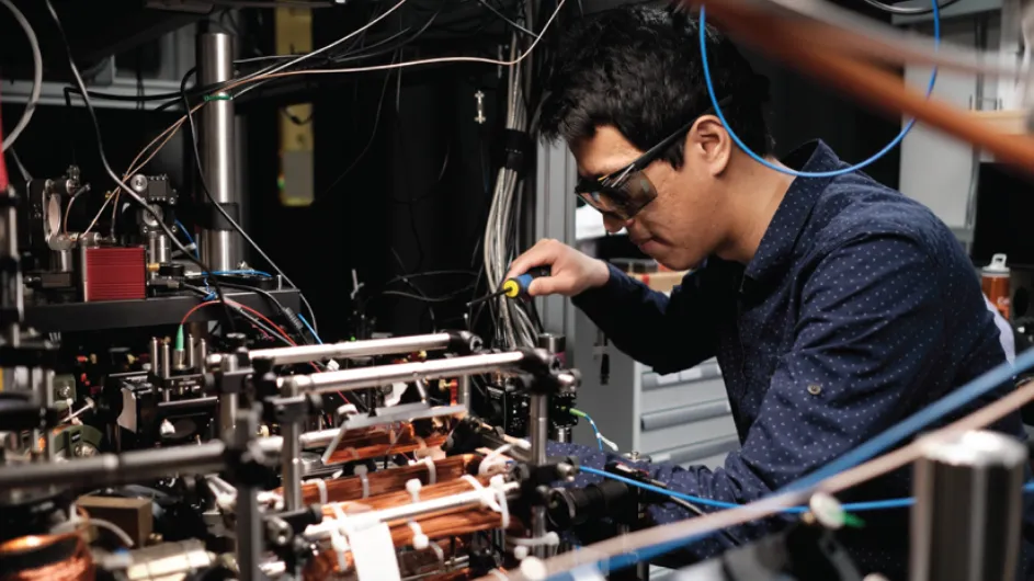 Columbia physicist Zhenjie Yan, wearing goggles and leaning over an optical table. 