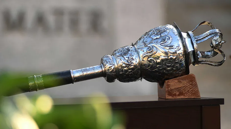 A roughly two-foot long wooden and silver-plated mace, adorned with acanthus leaves and topped with a crown, propped on a table in front of the statue of Alma Mater at Columbia University’s Commencement.