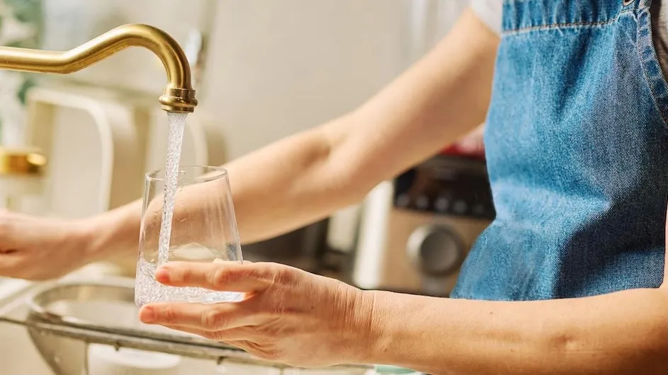 A person filling a glass of water from the tap