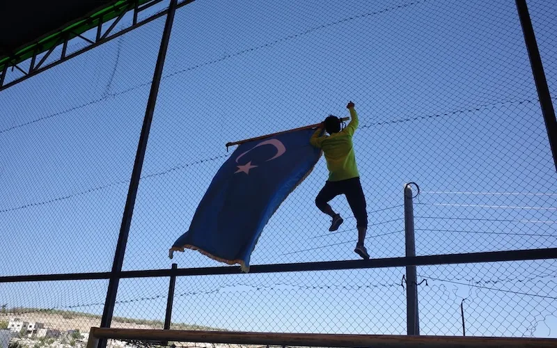 A Uyghur fighter in Syria climbs a fence to show the Uyghur flag. Photo by Emily Feng.