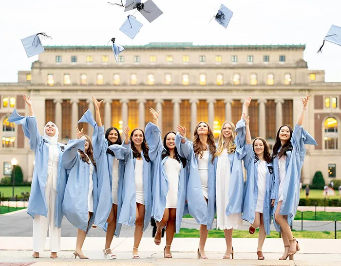 A group of grads throw their caps on the sundial in front of Butler Library.
