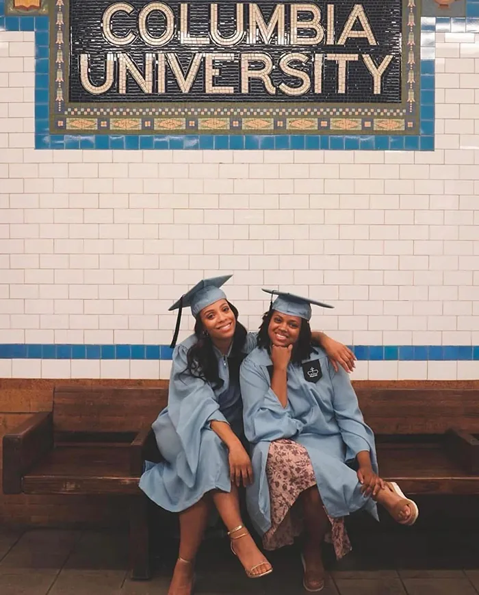 Two grads pose under the Columbia University subway tiles at the 116th station.