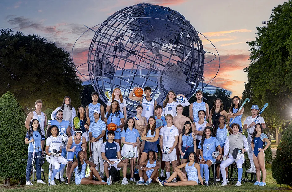Thirty-three university student-athletes in Columbia University sports uniforms pose in front of the Unisphere in Queens, New York City, at dusk.
