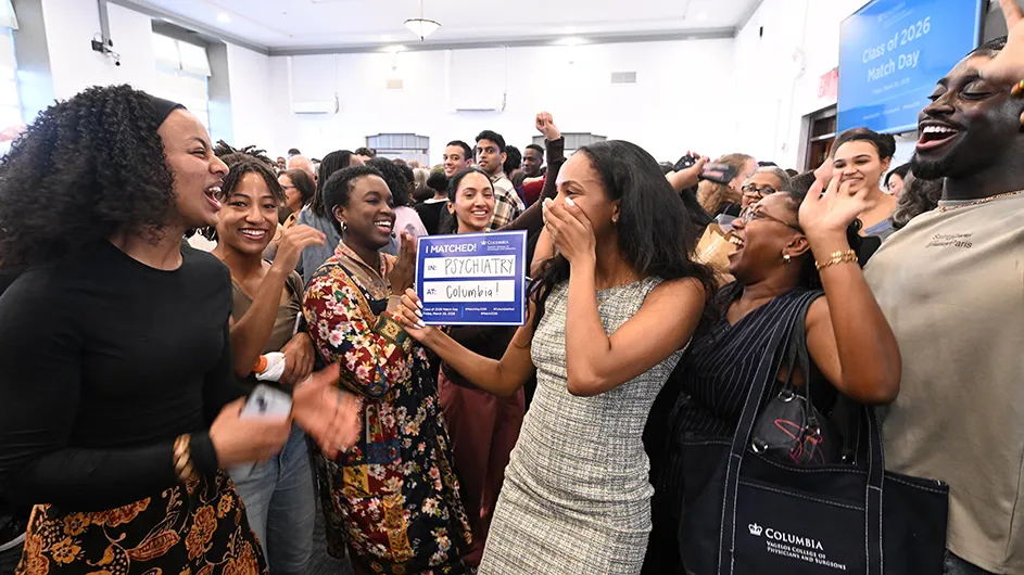 Several medical students with family members and friends joyfully celebrate Match Day news at Columbia University Irving Medical Center, with one medical student holding a "Match" card displaying the words "Psychiatry" and "Columbia" in the middle of the group.