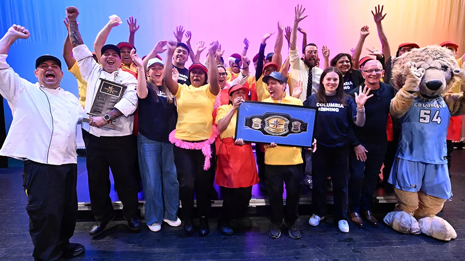 Several university students, Columbia lion mascot, chefs, and dining staff members celebrate and pose with dining awards for two top prizes at Columbia University's Battle of the Dining Halls.