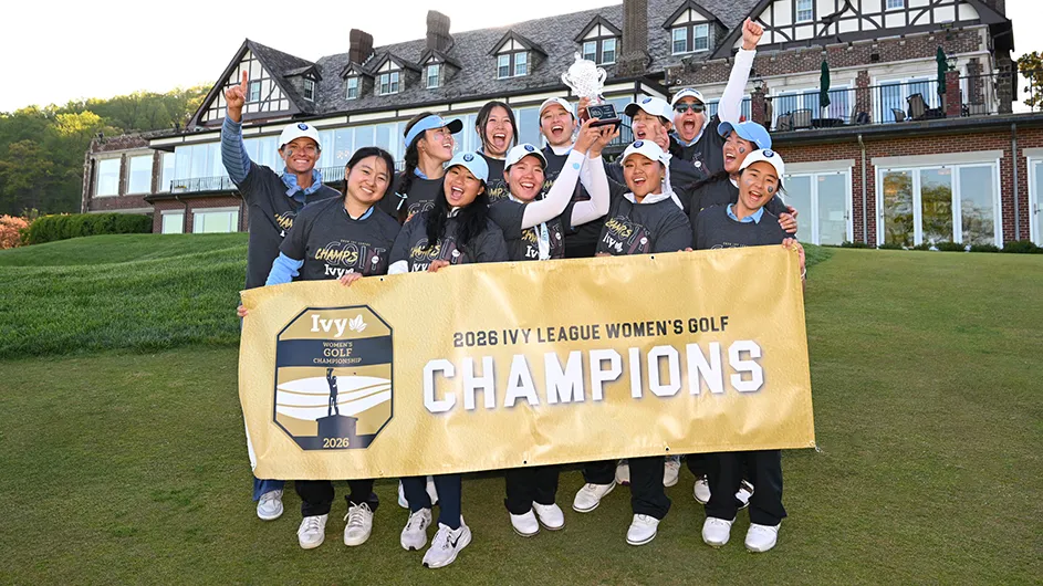 Twelve Columbia University student-athletes and coaches in athletic golf uniforms cheer and smile while celebrating with a trophy and a championship banner for the Ivy League Women's Golf Championships.