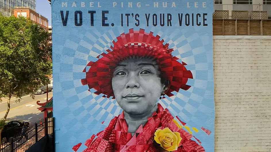 A huge public mural features pioneering suffragist Mabel Ping-Hua Lee wearing a red hat and coat with yellow rose under the letters “Vote. It’s your voice” on a brick wall next to a tree-lined street in Washington, D.C.
