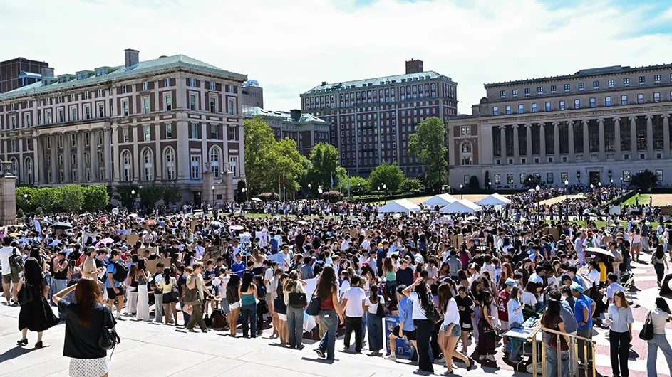 Hundreds of university students mingle and inquire about clubs and organizations at dozens of tables set up on Low Plaza, College Walk, and South Lawn with Butler Library, John Jay Hall, and Hamilton Hall in the background on a warm sunny day at Columbia University.