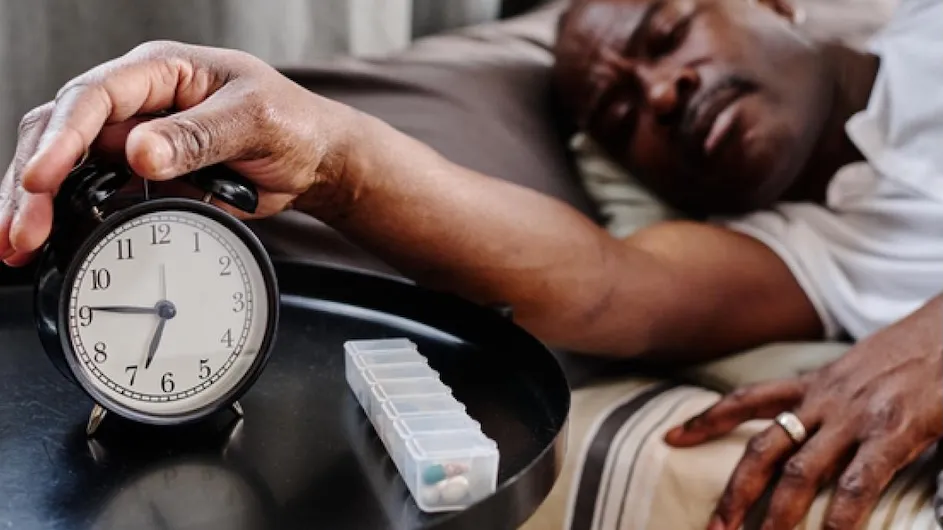 Image of a person hitting an alarm clock from bed.