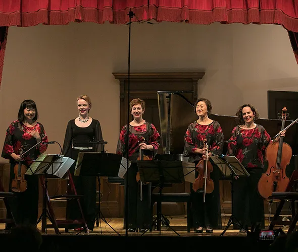 Five women, one dressed in black, on stage.