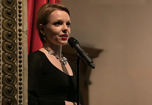 Magdalena Baczewska: woman with short blond hair, dressed in black and wearing a silver-colored necklace singing into a mic.