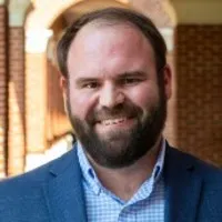 Robert Colby: A man with brown hair and beard, smiling, wearing a blue suit jacket and blue button-down shirt.