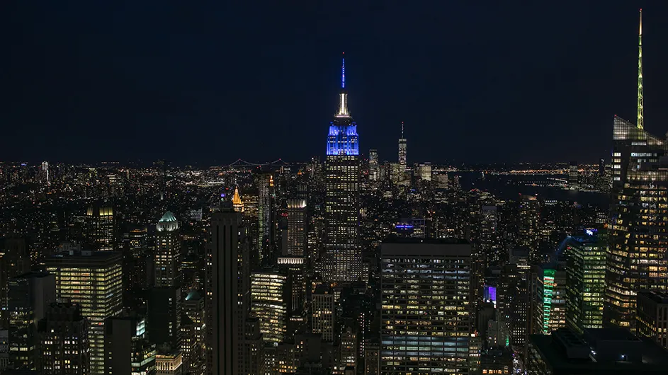 New York City skyline at night with the Empire State Building lit blue.