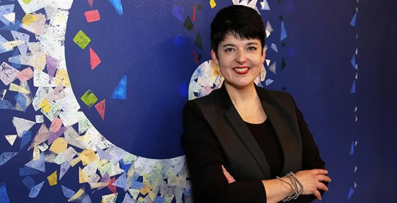 Deborah Cullen in dark suit arms crossed standing in front of colorful backdrop