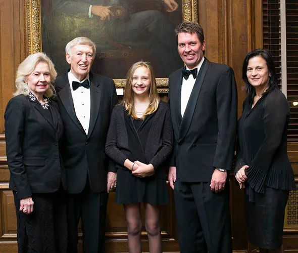 Five people dressed in black formal wear standing and posing in front of a picture