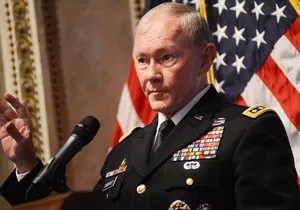 Wearing a military uniform studded with medals, a man stands at a podium speaking