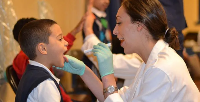 Doctor kneels infront of a small boy and shines a light in his mouth