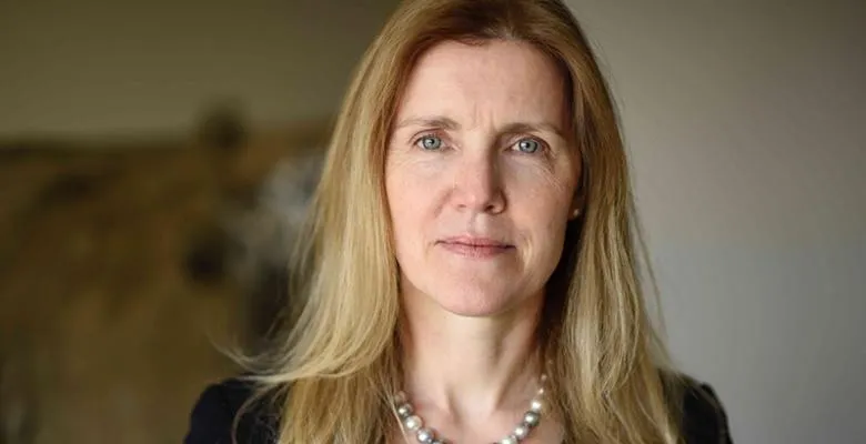 A woman with shoulder-length hair and wearing a string of pearls looks directly into the camera