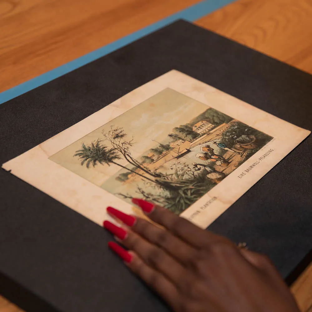 A photo of an old illustration of a town with a pond and a palm tree with a woman's hand holding the image