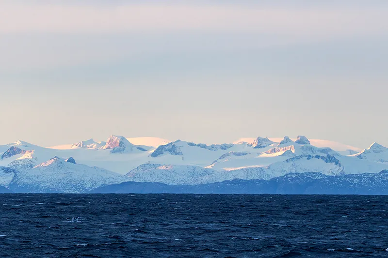 The white and blue landscape of the snowy Patagonian mountains by the ocean.