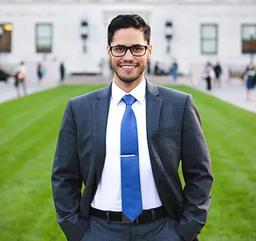 Brian Ruiz in a navy blue suit and tie, standing on a green lawn in front of Butler Library.
