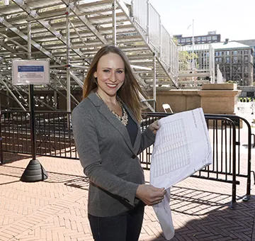 Mary Waldorf in a gray blazer, holding up blueprints. 