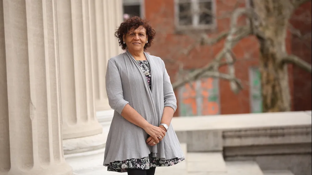 Woman with curly dark hair in grey dress standing next to columns