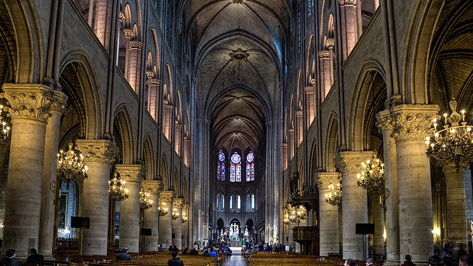 A perspective angle of inside Notre Dame with pews, columns, and a part of the arched cieling.