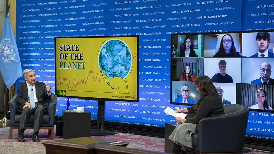 A World Leaders event at Columbia's Low Library in UN Secretary-General António Guterres,  an older man in a gray suit and light blue tie, sits in a chair on stage with Maureen Raymo, interim director at Columbia University’s Lamont-Doherty Earth Observatory, a woman with long dark hair, a dark suit jacket and gray skirt. On the stage are two large monitors one advertising the "State of the Planet" report  and the other a nine panel grid featuring virtual participants. 