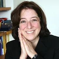 Anya Schiffrin in a black blazer with her hands clasped by her face