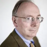 Richard R. John in a brown suit looking into the camera.