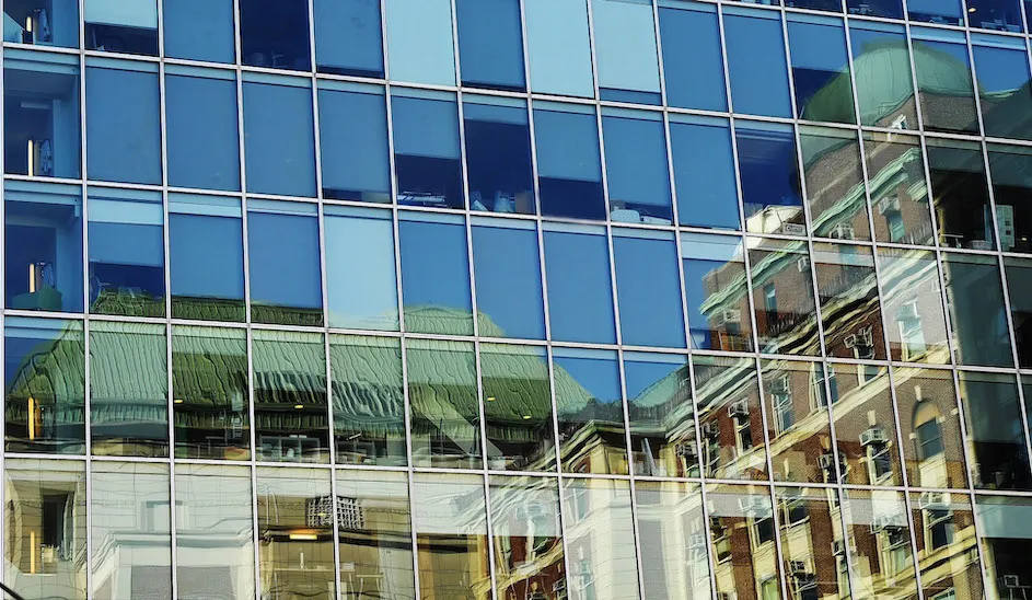 A photo of the side of a mirrored building reflecting an image of what looks like an older building