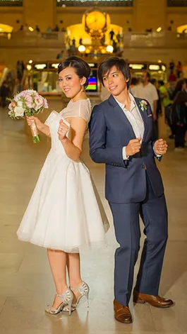 Two women, wife and wife, dance in a wedding dress and suit in Grand Central Station.