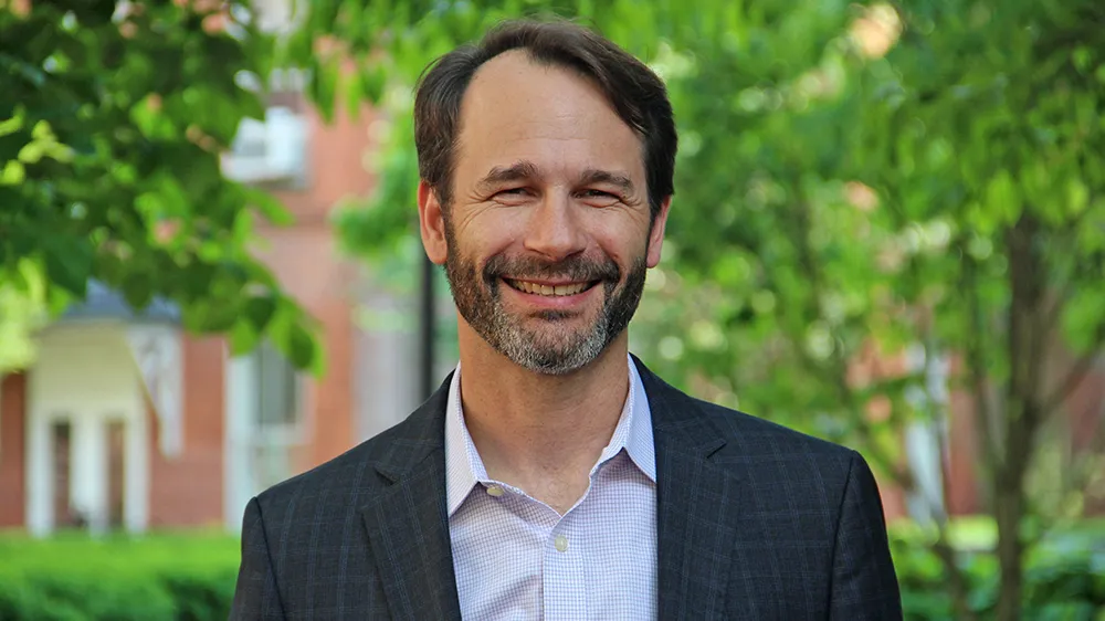 A bearded man smiling in front of green trees