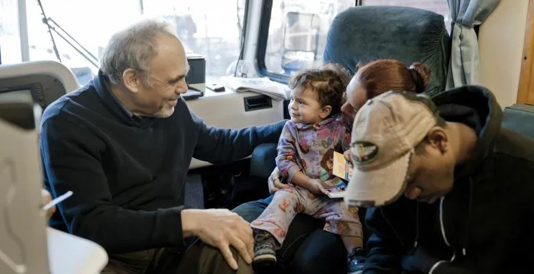 A small child sitting on her mother's lap smiles at Irwin Redlener.