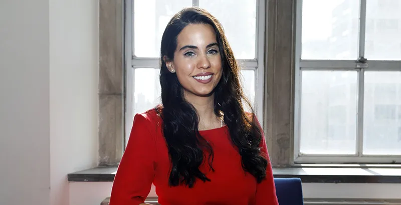 Linda Amrou in a red dress sitting in front of a bright window