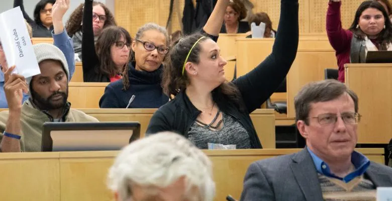 Sitting in chairs in a seminar room, people vote by raising their hands.