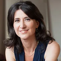 Marni Sommer: A woman with long dark hair and sleeveless, v-neck, dark shirt with a silver chain necklace and silver earrings, staring into the camera..