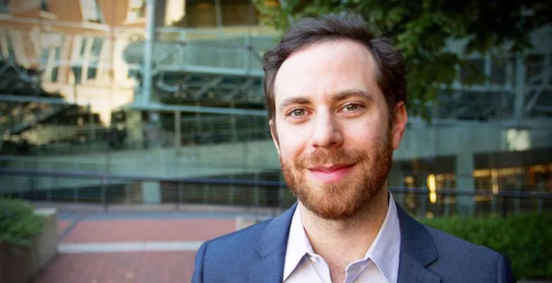 Close-up photo of Michael Slepian in a navy blue blazer standing in front the Lerner Hall's glass exterior