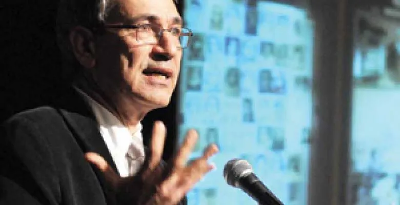 Man with grey hair and glasses gesticulates during a presentation