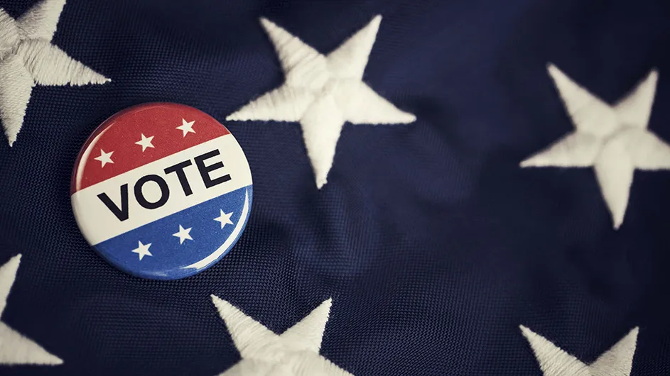 A red, white and blue pin with the word "vote" on it pinned to an American flag.