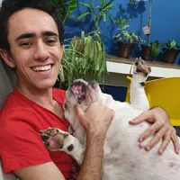 young man with black and red short, smiling, holding a white dog