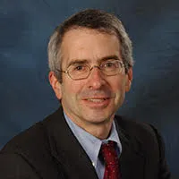 A bespectacled man smiling