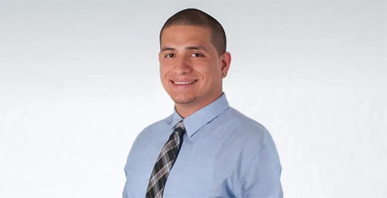 Richard Gamarra dressed in a light blue button down shirt with a navy plaid tie